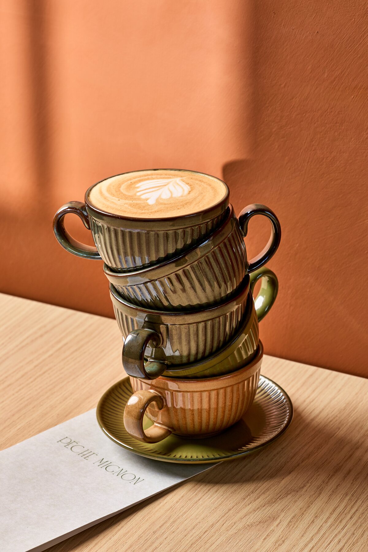 Stack of ceramic coffee cups topped with latte art on a café table at Péché Mignon