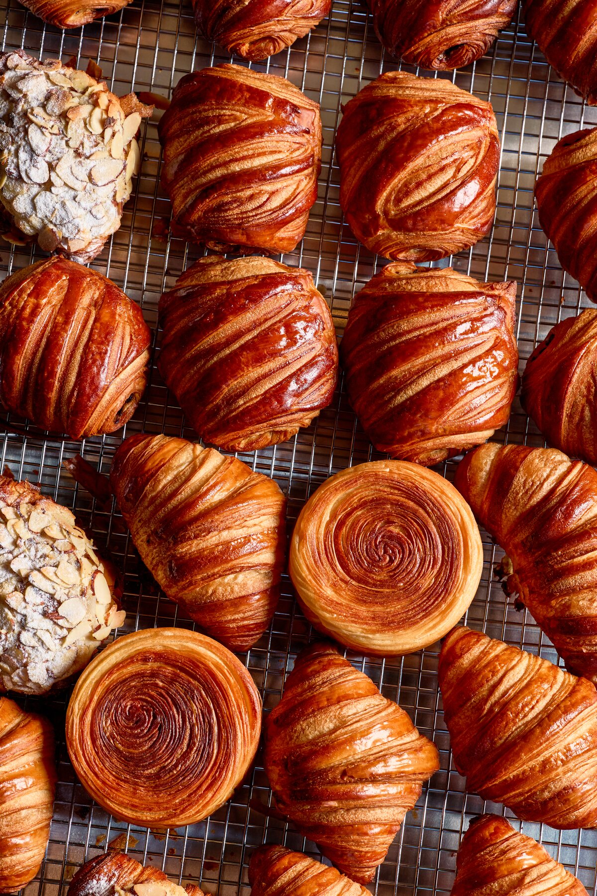 Assorted laminated pastries, croissants, and almond croissants cooling on wire racks at Péché Mignon